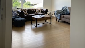Un salon spacieux avec une grande fenêtre, un canapé en cuir, une table basse en bois et un divan gris.