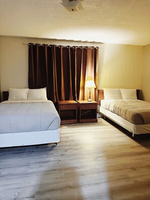 Habitación de hotel con dos camas, una mesita de noche, una lámpara y una cortina.