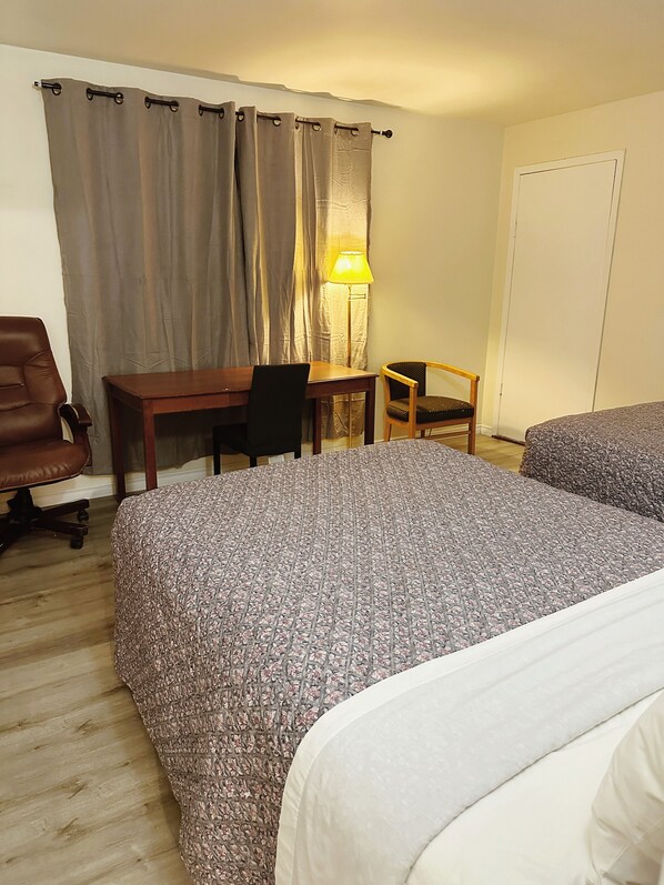 A hotel room with two beds, a desk, a chair, a lamp, and a wardrobe. - Uptown Motel (Estevan)