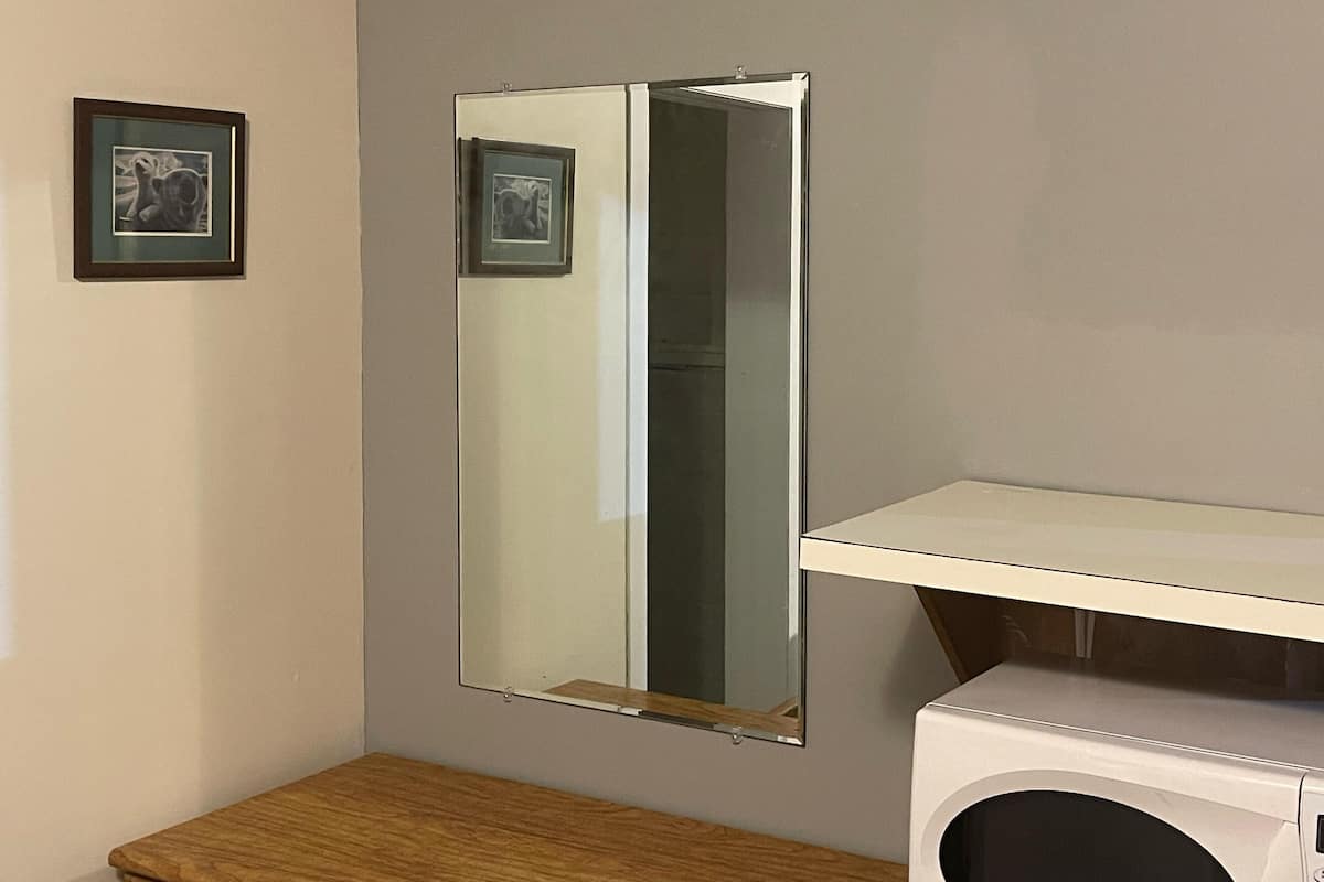 Une salle de bain avec un miroir, un tableau encadré, un banc en bois et un lave-linge.