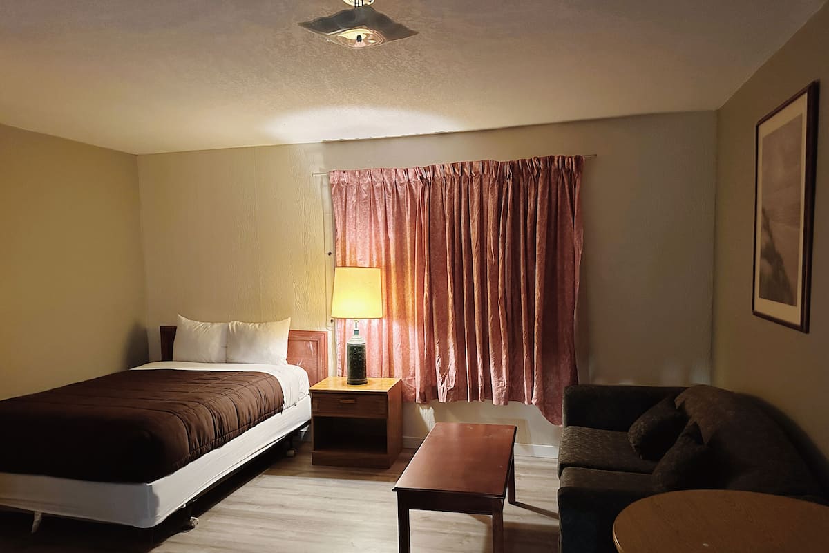Une chambre d’hôtel avec un lit, une table de chevet, une table, un canapé et une fenêtre avec des rideaux.