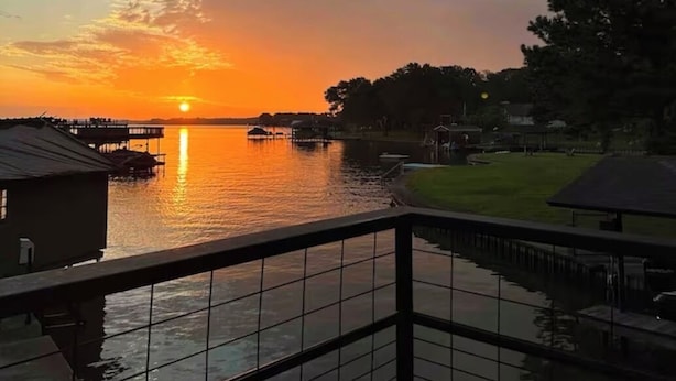 A sunset view from a balcony overlooking a calm body of water with a dock and buildings in the background.