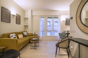 A modern living room with a sofa, a dining table, and chairs. There is a large mirror on the wall and a window with curtains. - Repubblica Suites (Milan)