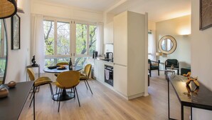A modern kitchen with a dining area, large windows, and a view of trees.