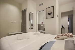 A hotel room with a large bed, a bedside table, a mirror, a framed picture, and a bathroom visible through an open door. - Repubblica Suites (Milan)