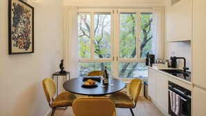 A compact kitchen with a dining area, large windows, and a view of trees.