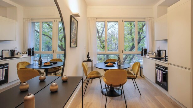 A modern kitchen with a dining area, large windows, and wooden flooring.