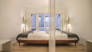 A bedroom with a large bed, bedside tables, a window with curtains, and wall-mounted lights.