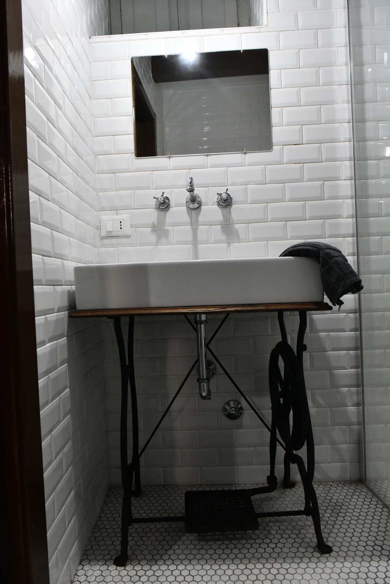 A bathroom with a white subway tile wall, a rectangular sink with a wooden countertop, and a black metal standpipe.