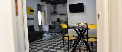 A compact kitchen with modern appliances, a dining area with yellow chairs, and a checkered floor.