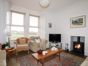 Ein Wohnzimmer mit einer Couch, einem Fernseher, einem Kamin und einem großen Fenster mit Jalousien.