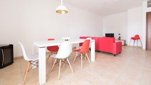 Ein modernes Wohnzimmer mit einem weißen Esstisch, roten und weißen Stühlen, einem roten Sofa und einem Fernseher.
