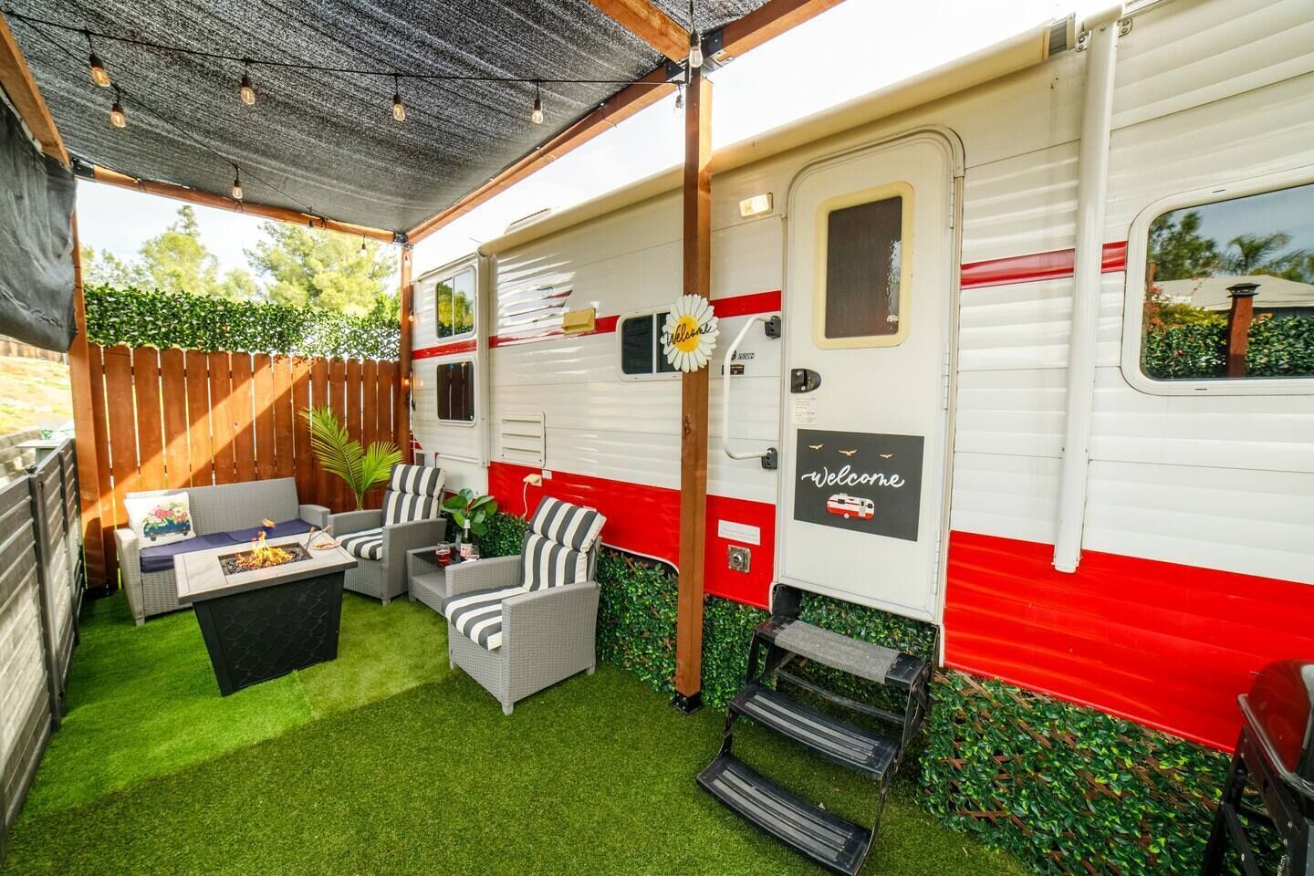 A caravan with a covered patio area, outdoor seating, and a small table with a fire pit.