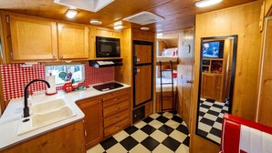 A compact kitchen with wooden cabinets, a microwave, and a sink. There is a checkered floor and a small window.