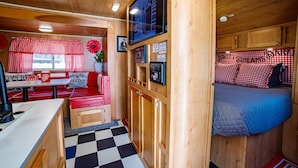 A cozy cabin interior with a kitchenette, a dining area, and a sleeping area with a bed and red checkered pillows.