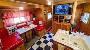 A cozy RV kitchen with a checkered floor, a dining area with red seating, and a television mounted above the sink.