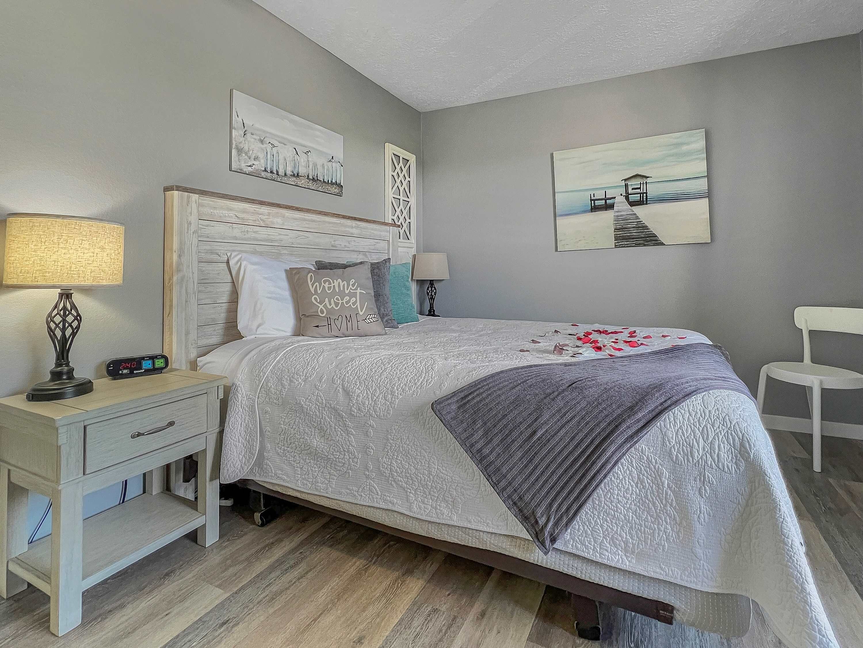 A bedroom with a bed, nightstand, lamp, and wall art.