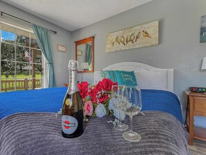 A bedroom with a bed, a bottle of Martini & Rossi wine, two wine glasses, and a bouquet of flowers.