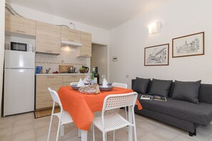 A modern kitchen with white cabinets, a dining table with an orange tablecloth, and a grey sofa.