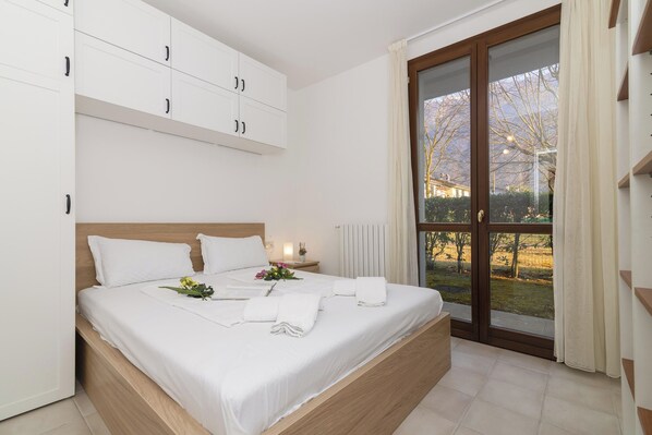 A bedroom with a bed, a nightstand, a window with a view, and a wardrobe.