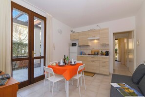 A modern kitchen with wooden cabinets, a dining area with a table and chairs, and a view through a glass door.