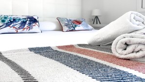A neatly made bed with a white towel, a colorful pillow, and a striped rug. - Payen Corralejo by Best Holidays Fuerteventura (Corralejo)