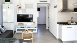 A modern living room with a flat-screen TV, a sofa, a coffee table, and a kitchen area with white cabinets and a stainless steel range hood. - Payen Corralejo by Best Holidays Fuerteventura (Corralejo)