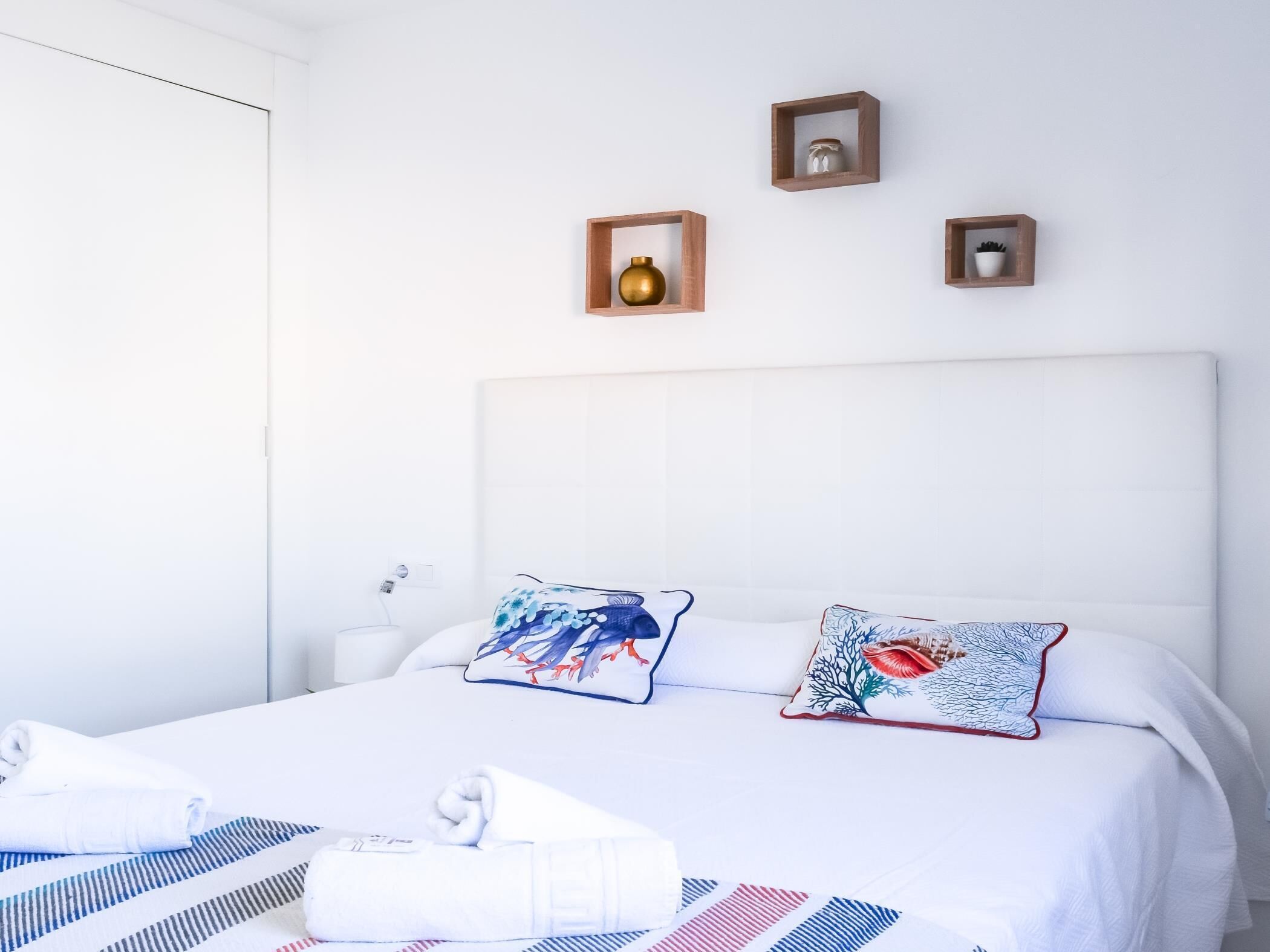 Una cama bien hecha con una colcha a rayas, dos almohadas decorativas y un juego de toallas a un lado.