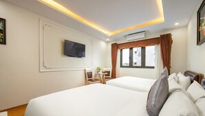 Une chambre d’hôtel avec deux lits, un téléviseur fixé au mur, une petite table avec des chaises et une fenêtre avec des rideaux.