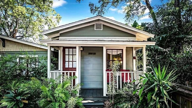 A two-story house with a porch, surrounded by lush greenery.