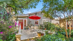 A wooden deck with a red umbrella, surrounded by lush greenery and potted plants.