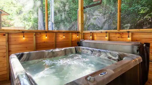 A wooden cabin with a hot tub and a view of the forest.