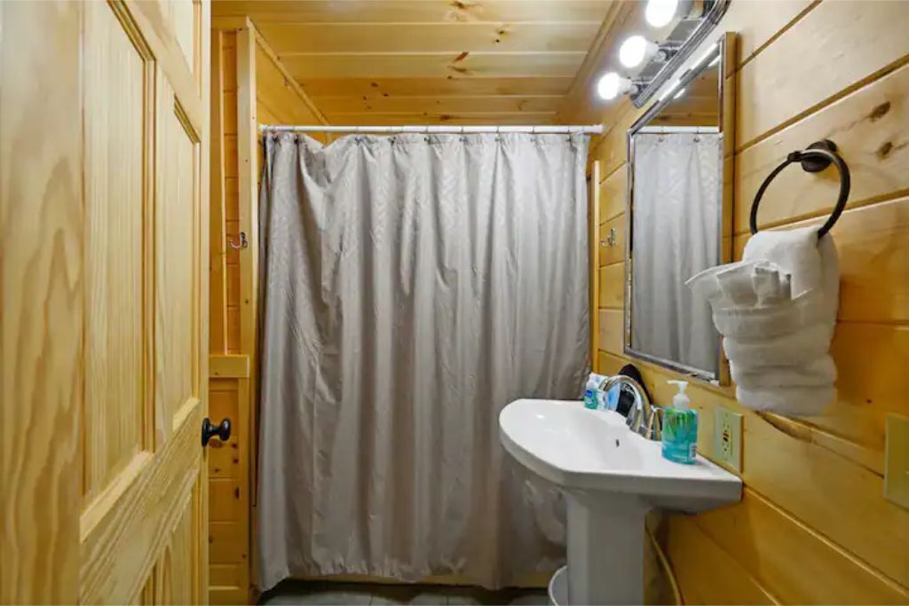Un baño de cabaña de madera con cortina de ducha, lavamanos y espejo.