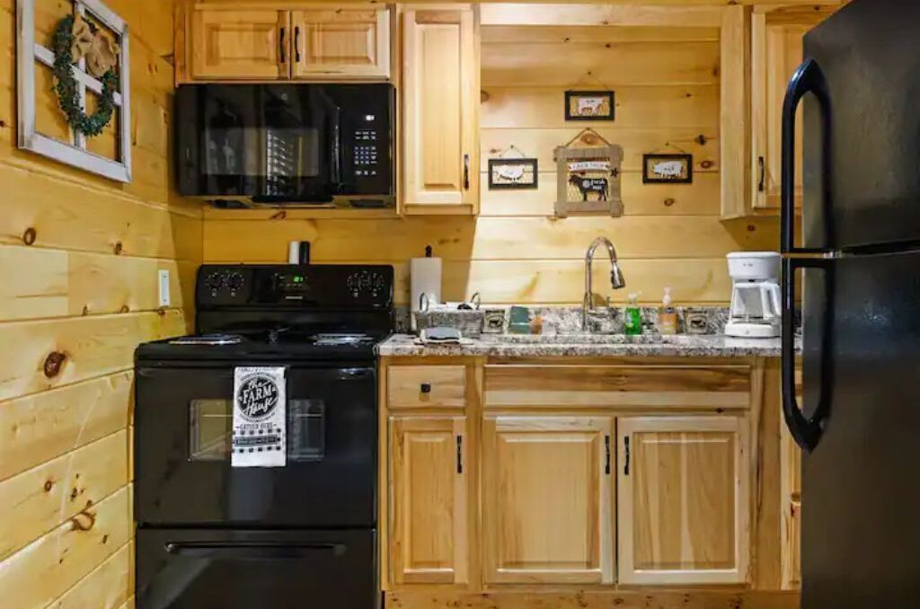 A kitchen with wooden cabinets, a black stove, a microwave, a sink, and a refrigerator.