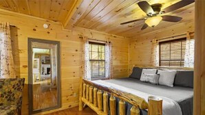 A log cabin bedroom with a bed, a chair, and a ceiling fan.