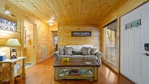 A cozy cabin interior with a wooden floor, a sofa, a coffee table, a lamp, and a sign that reads "Gather together love and laughter forever."