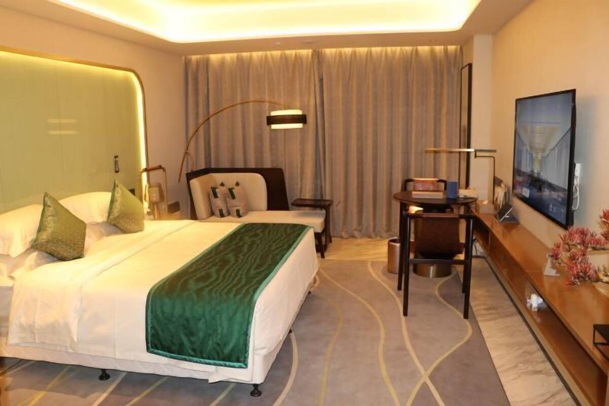Ein Hotelzimmer mit Bett, Schreibtisch, Stuhl, Lampe, Fernseher und einem Bild an der Wand.