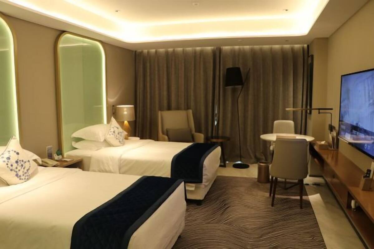 Ein Hotelzimmer mit zwei Betten, einem Fernseher, einem Schreibtisch und einem Stuhl.