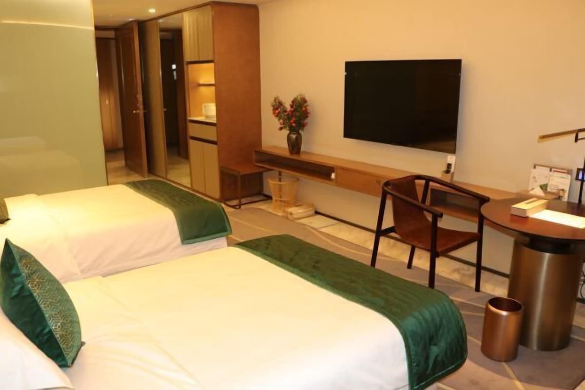 A hotel room with two beds, a desk, a chair, a TV, and a trash can.