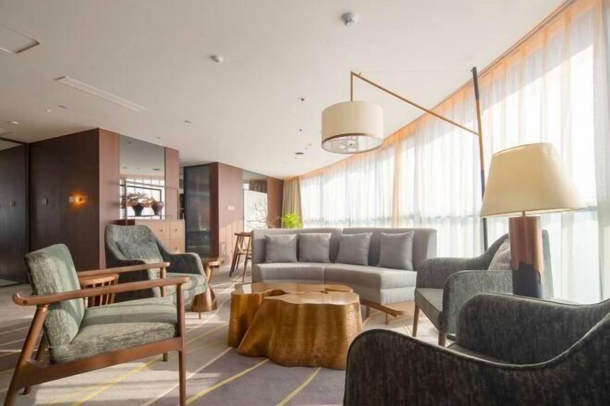 Eine moderne Hotelhalle mit einer Sofagarnitur, Sesseln, einem Couchtisch und einem großen Fenster mit Vorhängen.