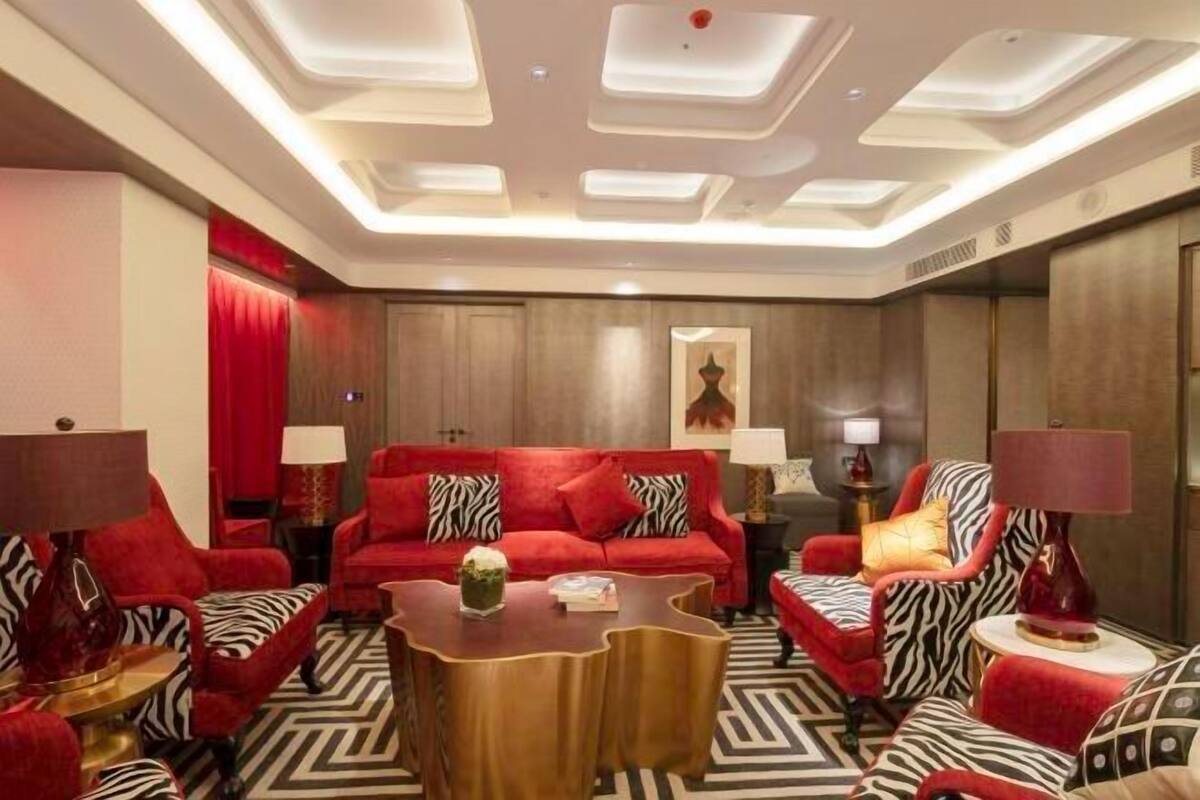 Ein modernes Hotelzimmer mit einer roten Sofagarnitur, einem Holztisch und einem gemusterten Teppich.