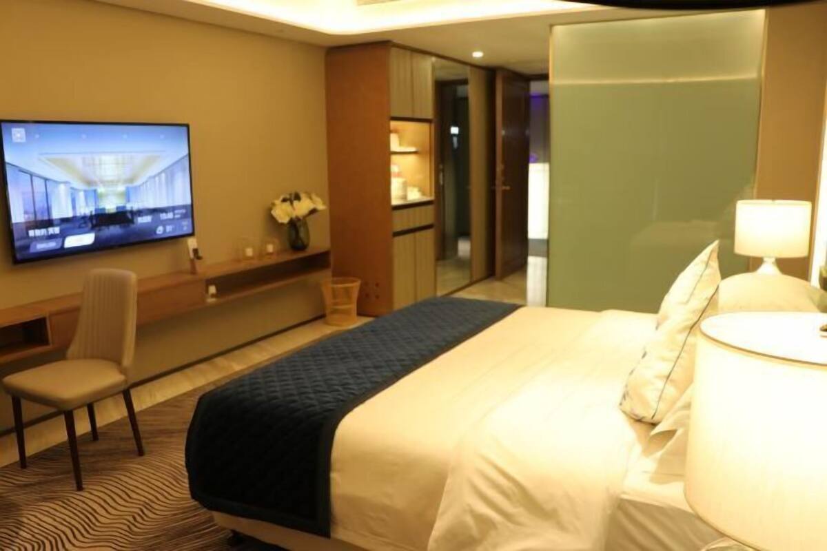 Ein Hotelzimmer mit Bett, Sessel, Wandfernseher und Nachttisch mit Lampe.