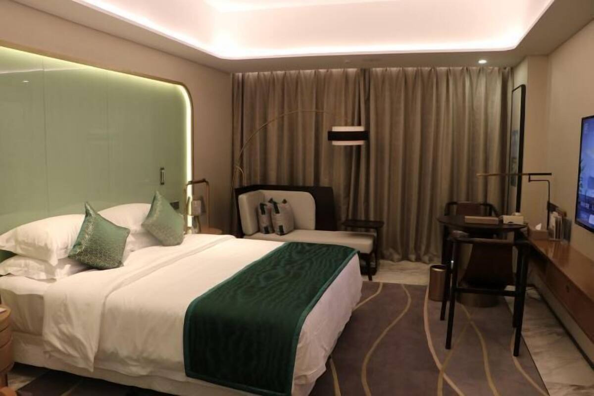 Ein Hotelzimmer mit Bett, Schreibtisch, Stuhl, Fernseher und einem großen Fenster mit Vorhängen.