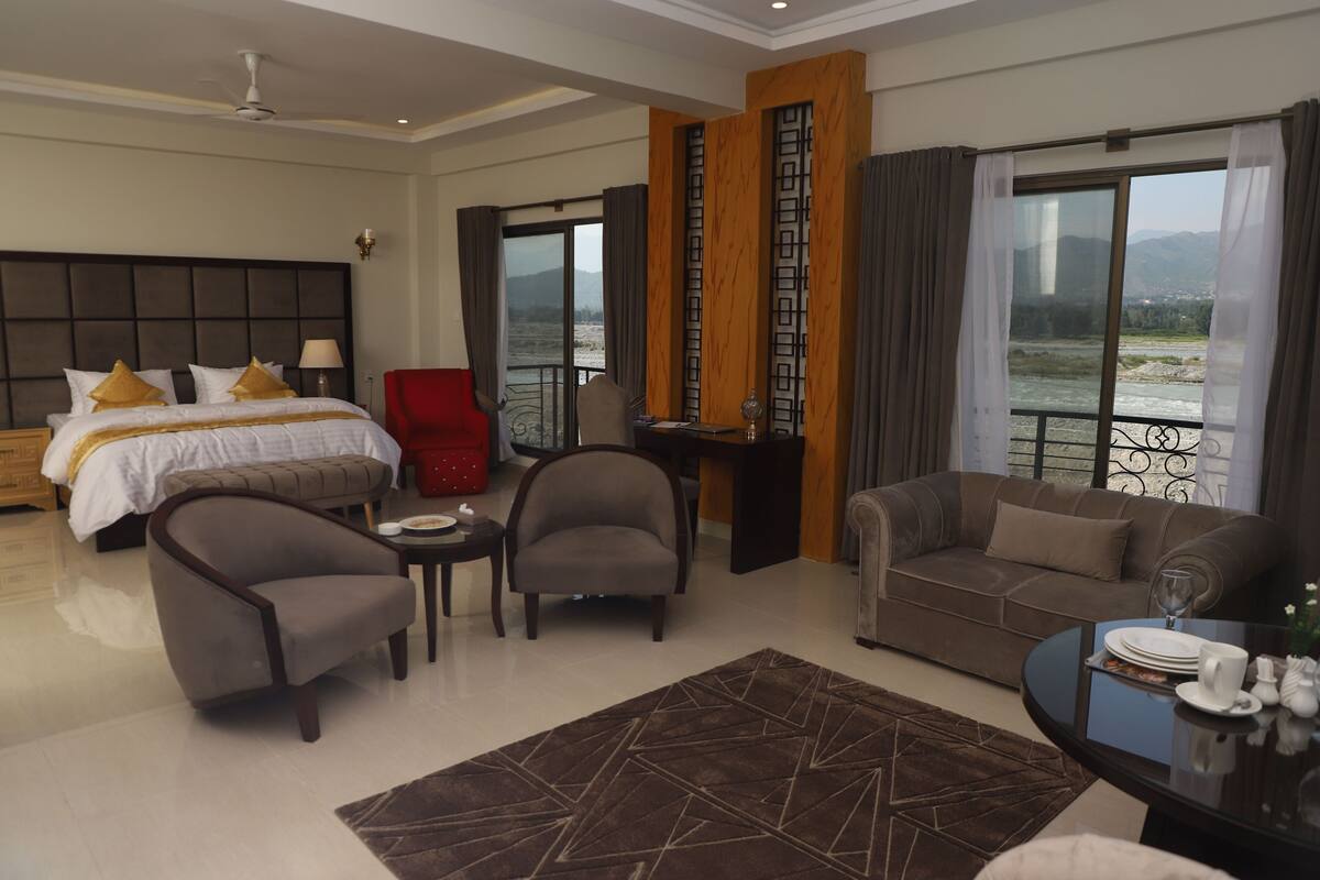Une chambre d’hôtel comprenant un lit, deux fauteuils, un canapé, une table à manger et une vue sur une rivière.