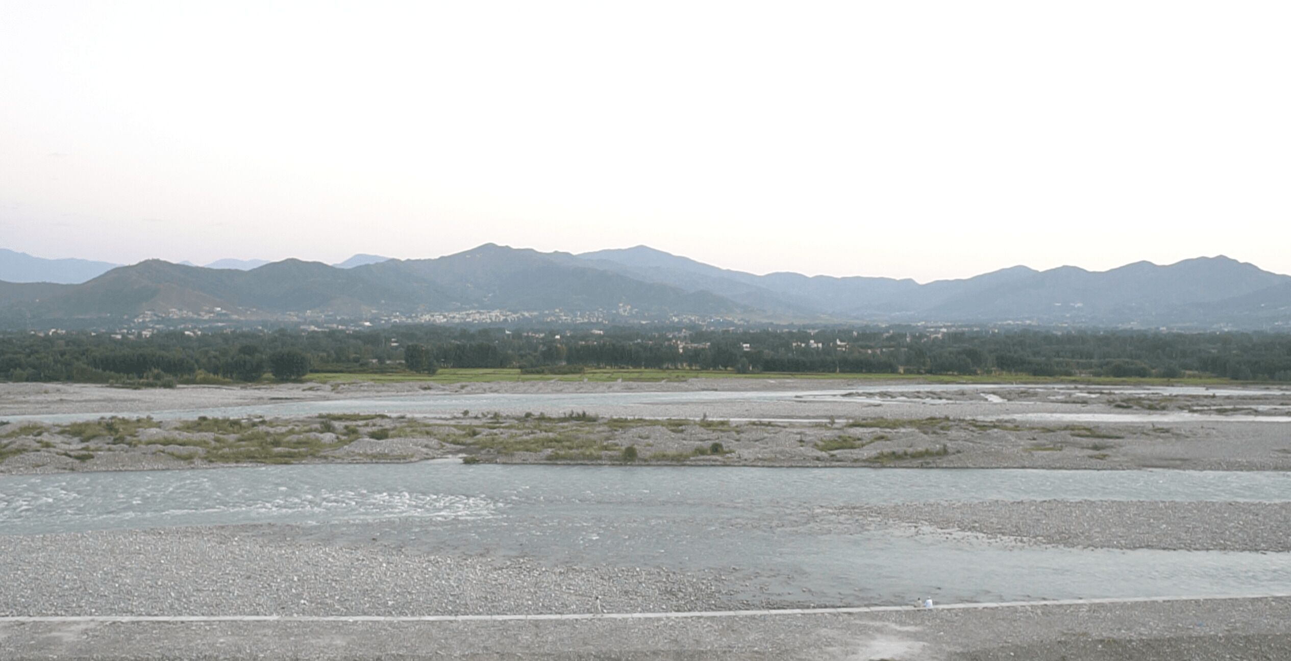A flat, open landscape with distant mountains and a small settlement.
