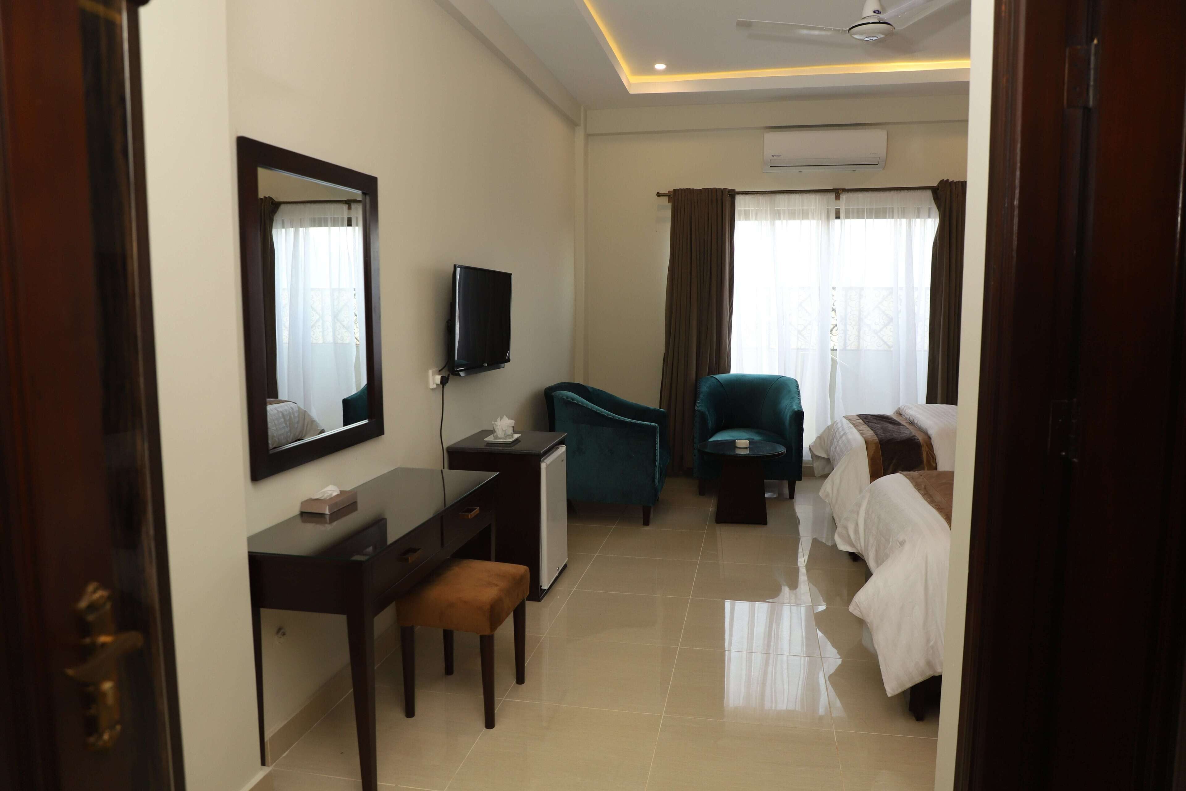 A hotel room with a desk, chair, television, and two beds.