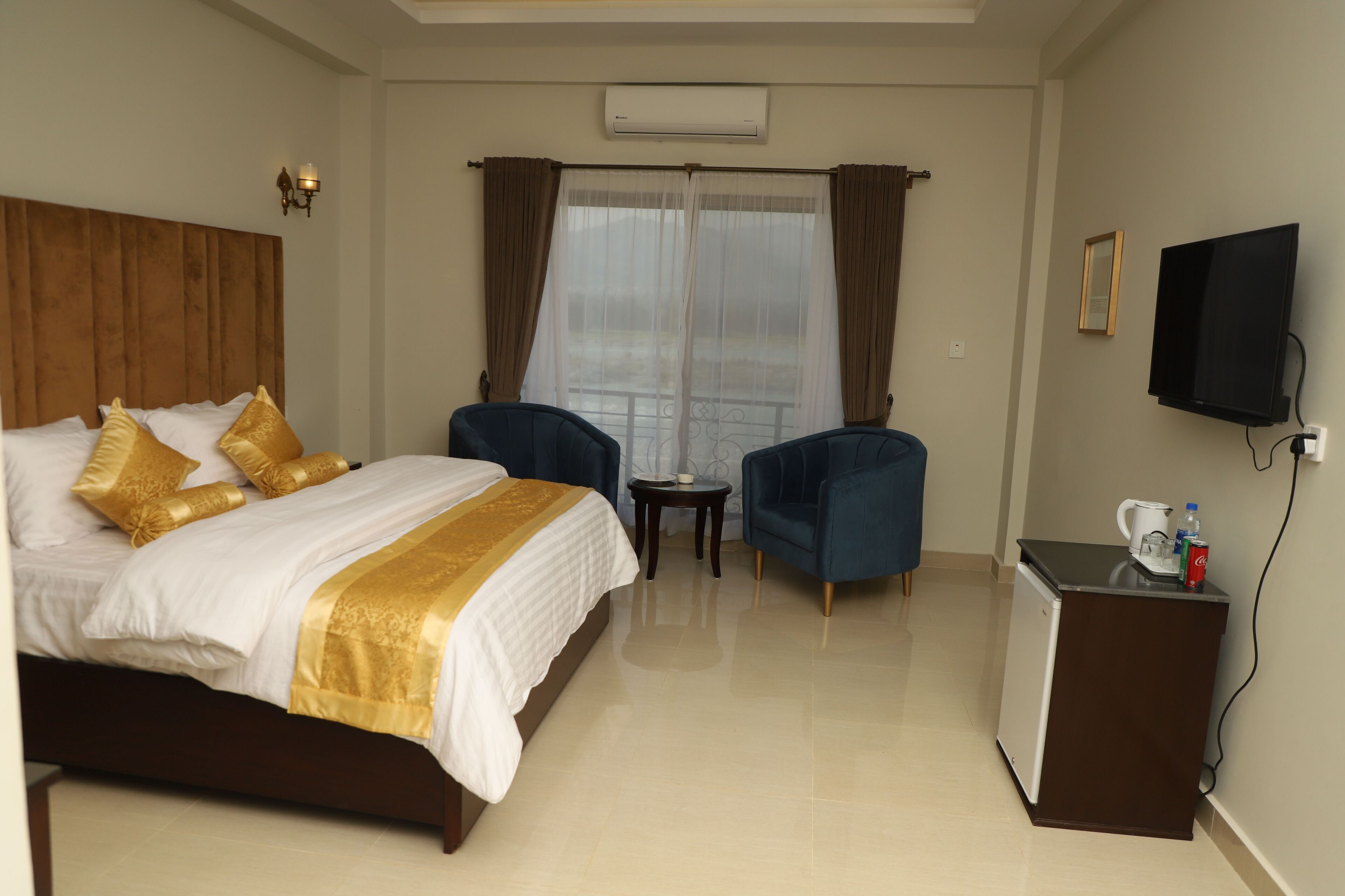 A hotel room with a bed, two armchairs, a small table, a television, and a minibar.