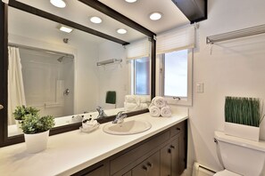 Un baño con un lavamanos blanco, un espejo grande, un perchero para toallas y un inodoro.