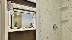 Une salle de bain avec un mur de douche en marbre, un meuble-lavabo avec un miroir et un évier.
