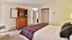 Une chambre à coucher comprenant un lit, une commode en bois, un téléviseur et un dressing.